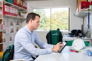 Man in een bouwkeet kijkend naar z'n tablet